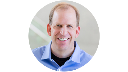 Portrait of Brian Cross smiling in a blue collared shirt with a neutral background