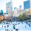 People skating on an ice rink in Central Park, surrounded by trees and city buildings, enjoying a winter day.