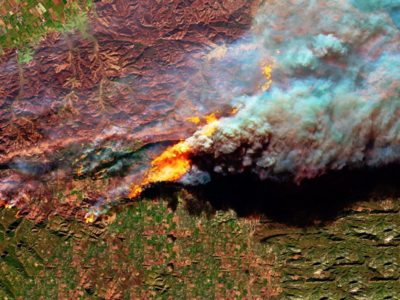 Aerial view of a wildfire burning in a green landscape