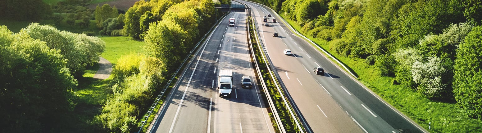 Aerial view of a broad tree-lined highway winding through bright green country hills
