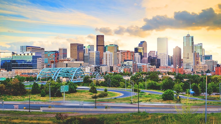 Aerial view of a sleek modern city with many bright green park spaces with skyscrapers reflecting the colors of a golden sunrise