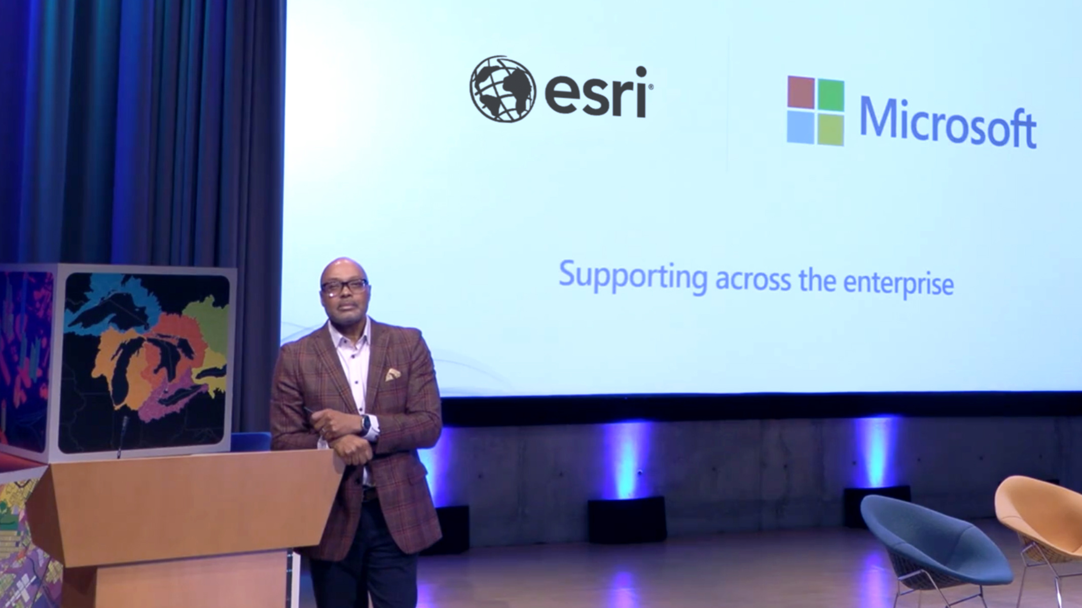 Person standing at a podium on a stage with a screen behind him showing the Esri and Microsoft logos
