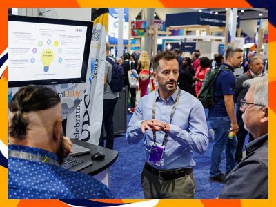 Presenter wearing business casual attire explains information displayed on a monitor to two others at an Expo booth