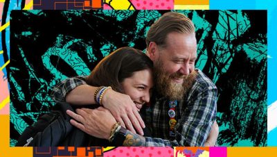 Smiling attendees embrace with one wearing a plaid shirt and Esri swag buttons and the other wearing a backpack