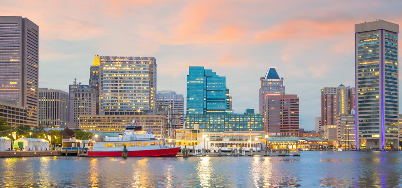 Panorama view of a bustling modern riverside city beginning to light up for nighttime under a soft orange and blue sunset sky