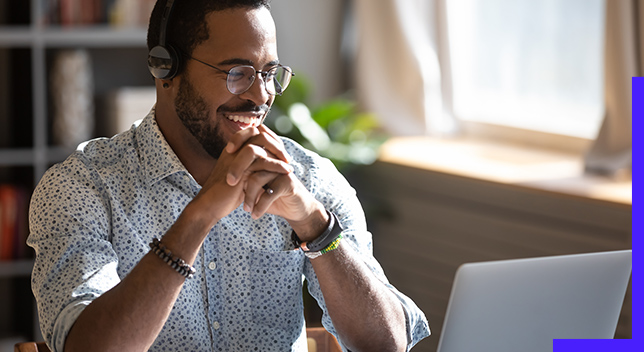 Person wearing glasses, seated at a desk, smiling and looking at a laptop screen