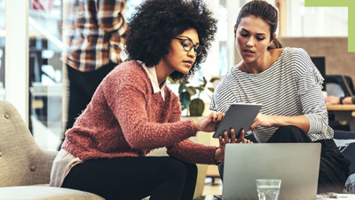 Two people sitting in a coffee shop working with GIS software on a tablet and laptop