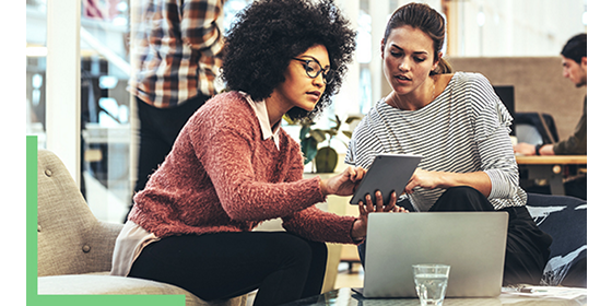 Two people sitting in a coffee shop working with GIS software on a tablet and laptop